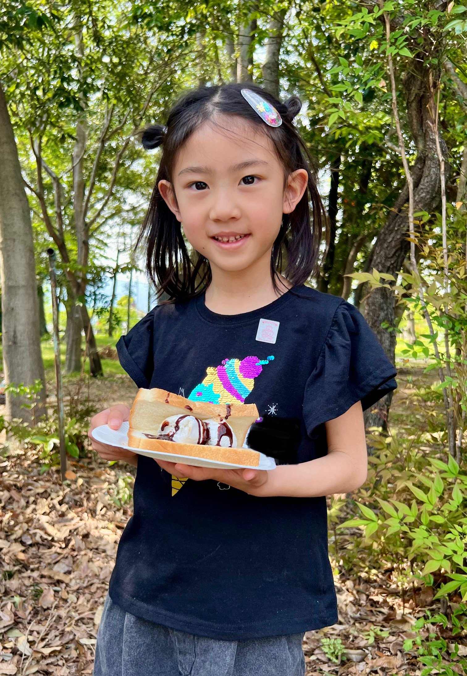 MiRAIヒミツ基地デイキャンプで、女の子が自分で作ったおやつを手に嬉しそうな笑顔を見せている様子。三重県四日市・菰野町を拠点にした子ども向け体験型習い事の一コマ。