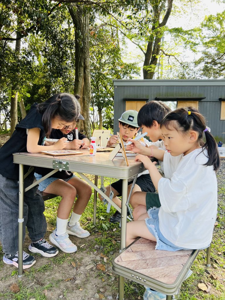 MiRAIヒミツ基地デイキャンプで、子どもたちが真剣にフォトフレームを創作し、思い出の集合写真を貼って完成させている様子。四日市・菰野町を拠点とした子ども向け体験型習い事の一場面。