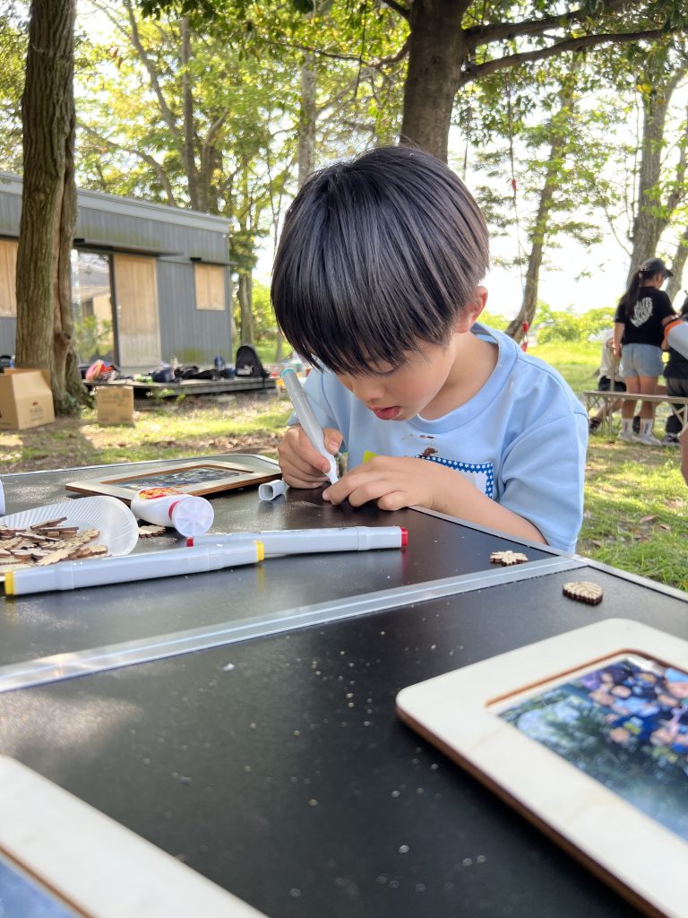 MiRAIヒミツ基地デイキャンプで、子どもたちが真剣にフォトフレームを創作し、思い出の集合写真を貼って完成させている様子。四日市・菰野町を拠点とした子ども向け体験型習い事の一場面。