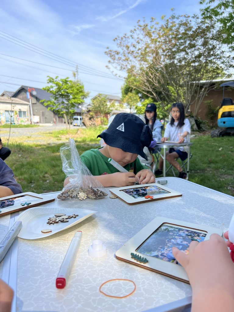 MiRAIヒミツ基地デイキャンプで、子どもたちが真剣にフォトフレームを創作し、思い出の集合写真を貼って完成させている様子。四日市・菰野町を拠点とした子ども向け体験型習い事の一場面。