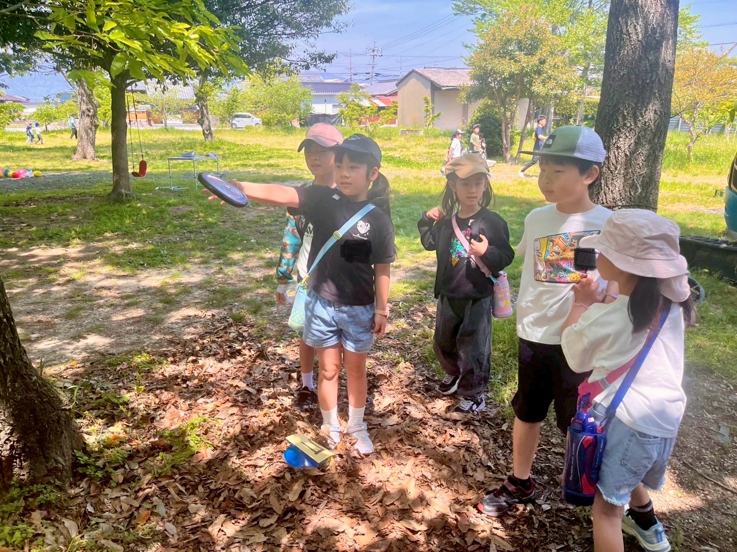 MiRAIヒミツ基地デイキャンプで、子どもたちがフリスビーを使ったディスクゴルフに挑戦し、友だちの投げる様子を祈るように応援して見守る様子（四日市・菰野町）