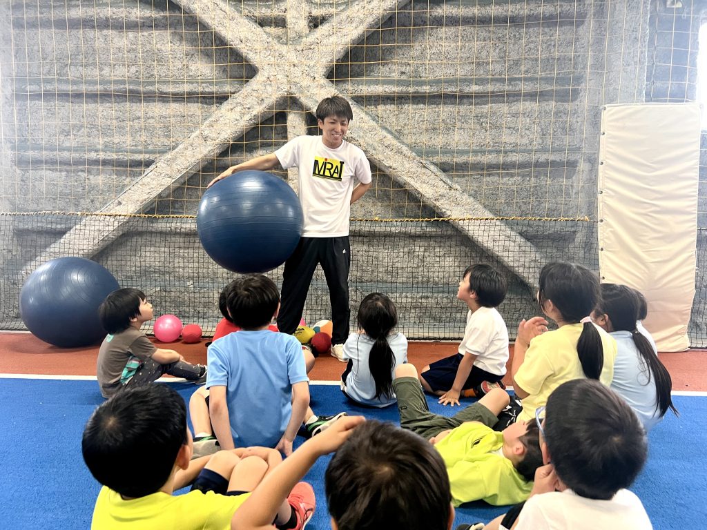 MiRAI体育スクールでけいた先生がバランスボールを手に、四日市の小学生たちに運動の目標を説明する様子