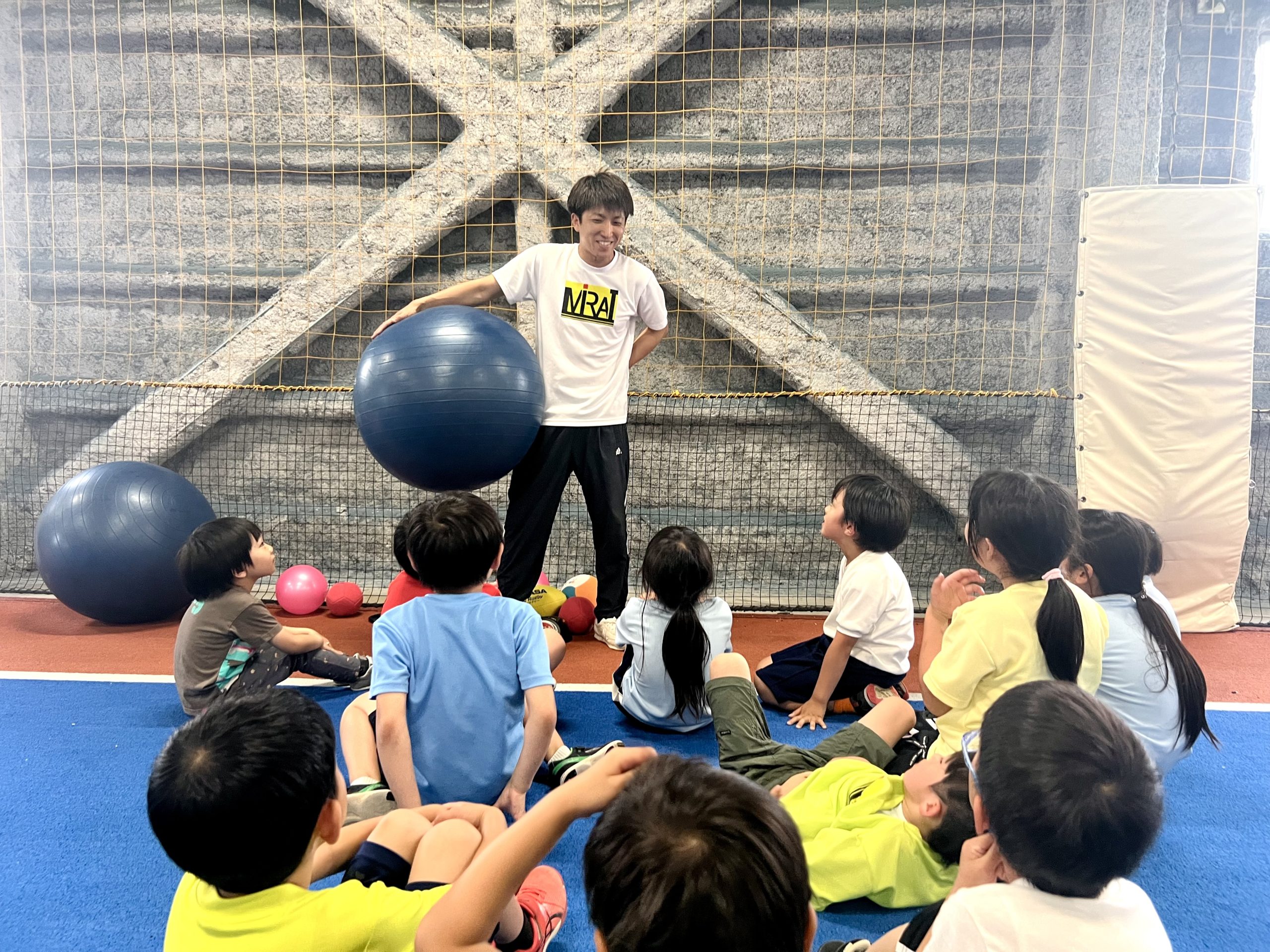 MiRAI体育スクールでけいた先生がバランスボールを手に、四日市の小学生たちに運動の目標を説明する様子