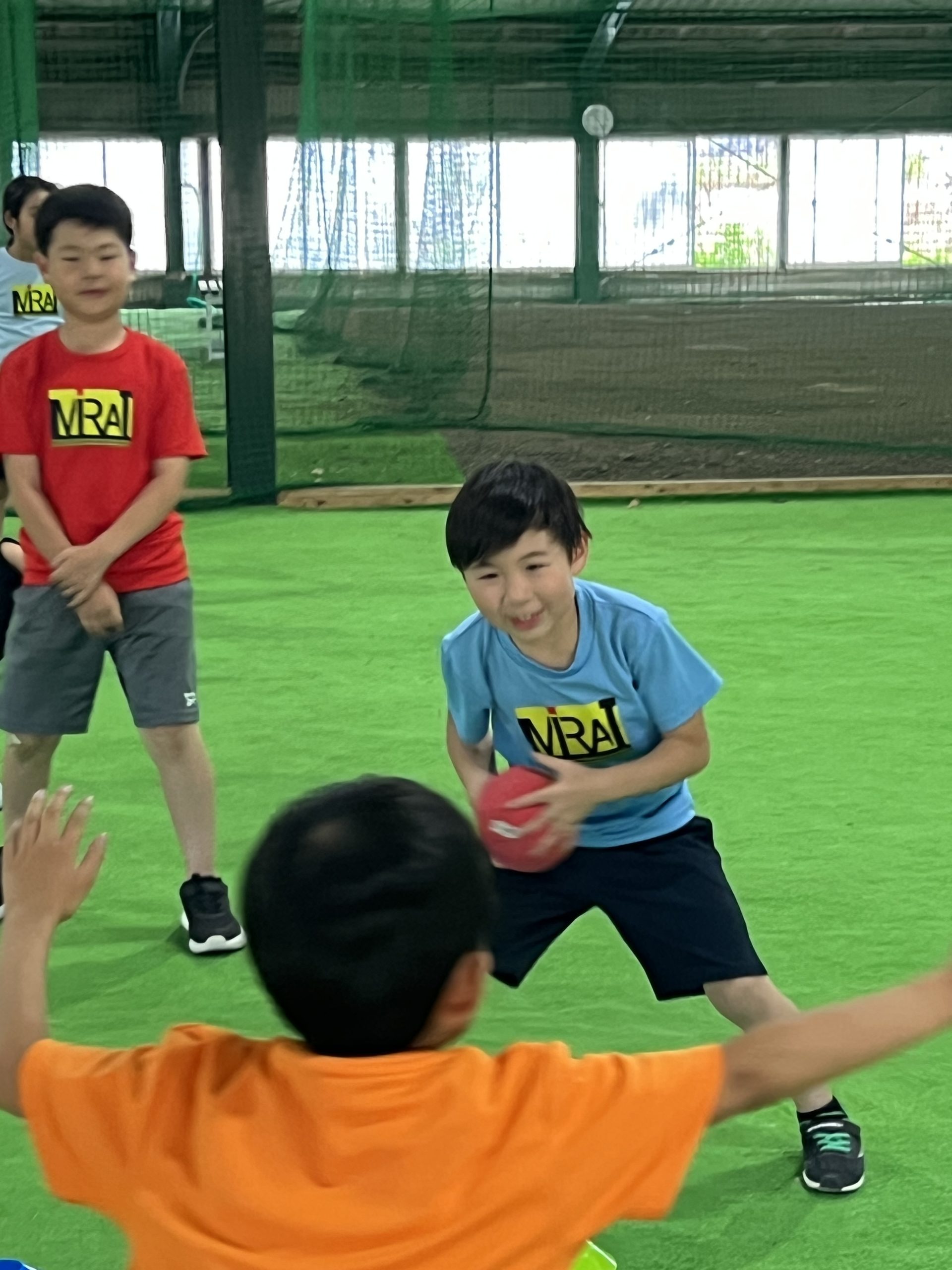 四日市市・あがたのMiRAIスポーツスクールで、子どもたちが初めてのハンドボールに挑戦している様子。横の動きで相手をかわし、スペースを見つけてシュートを狙うシーン。