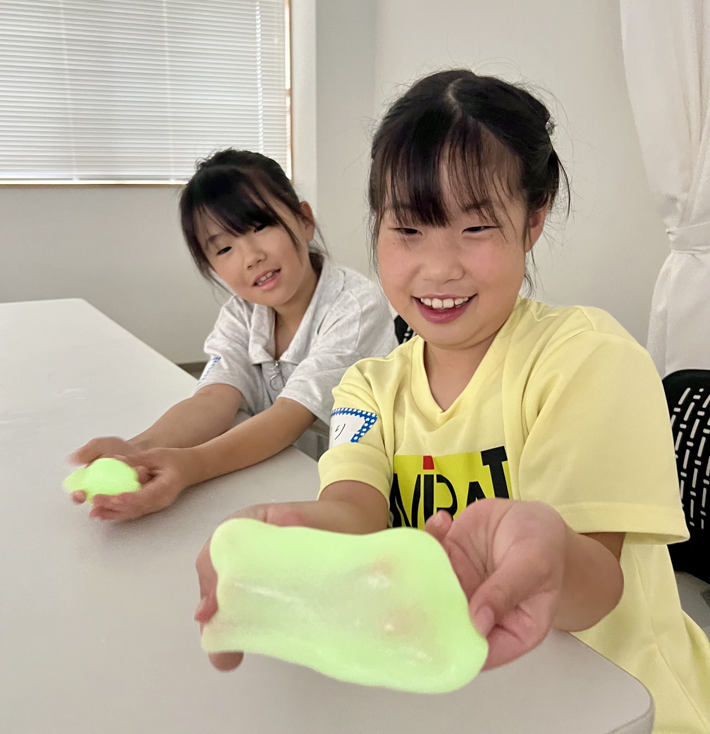 光るスライムを完成させて笑顔で見せる小学生の女の子たち｜四日市・子ども習い事・科学実験