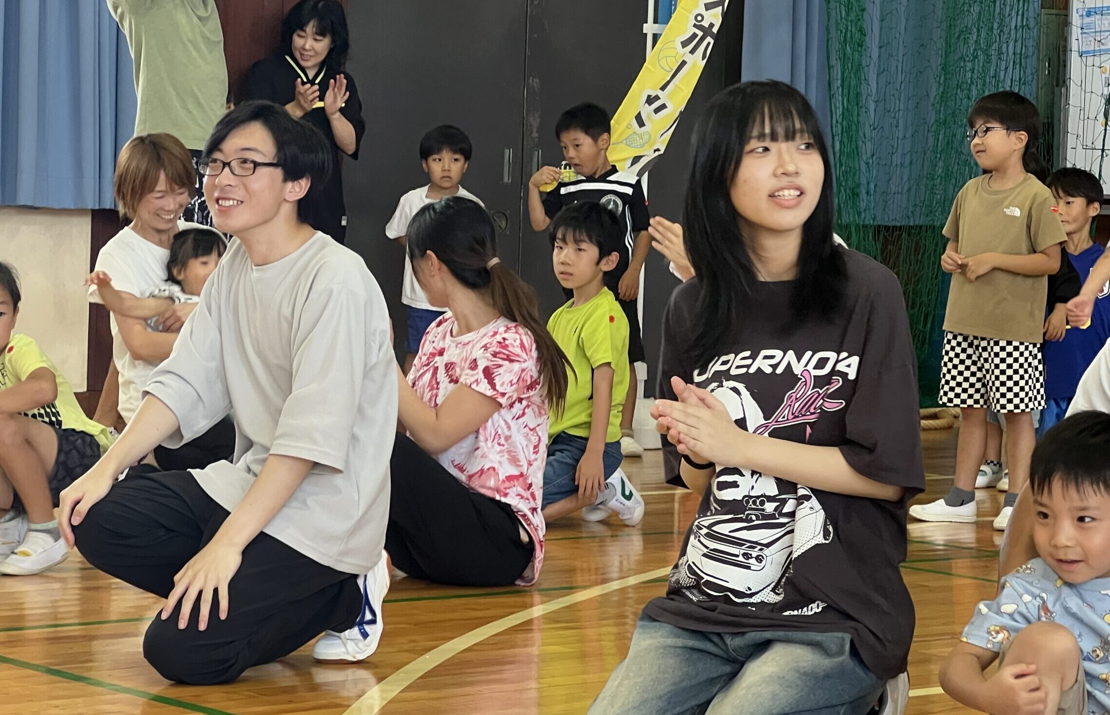 四日市メリノール学院の生徒がMiRAI親子運動会で競技中にしゃがんで子どもたちを応援している様子
