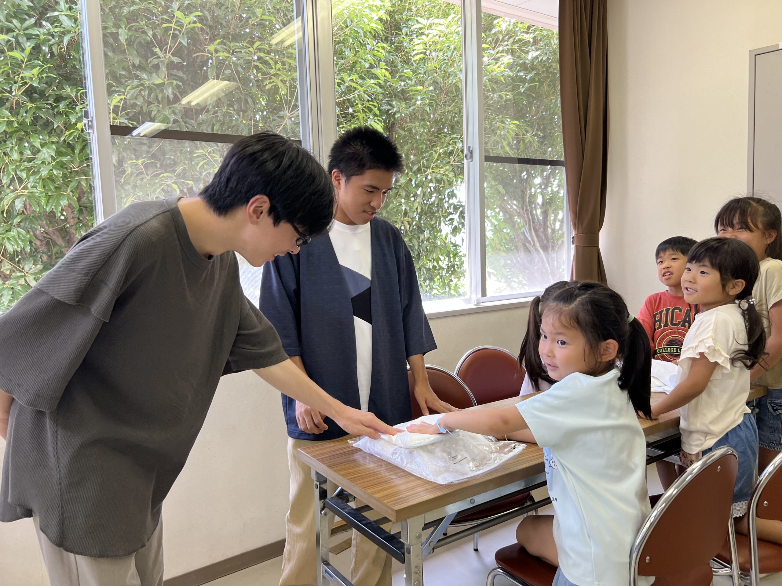 四日市のMiRAIサマスクで、メリノール学院の高校生ボランティアが小学生に寄り添って学習指導をしている様子。夏休みの1日を通じて安心できる環境で学びのサポートを受けている瞬間。