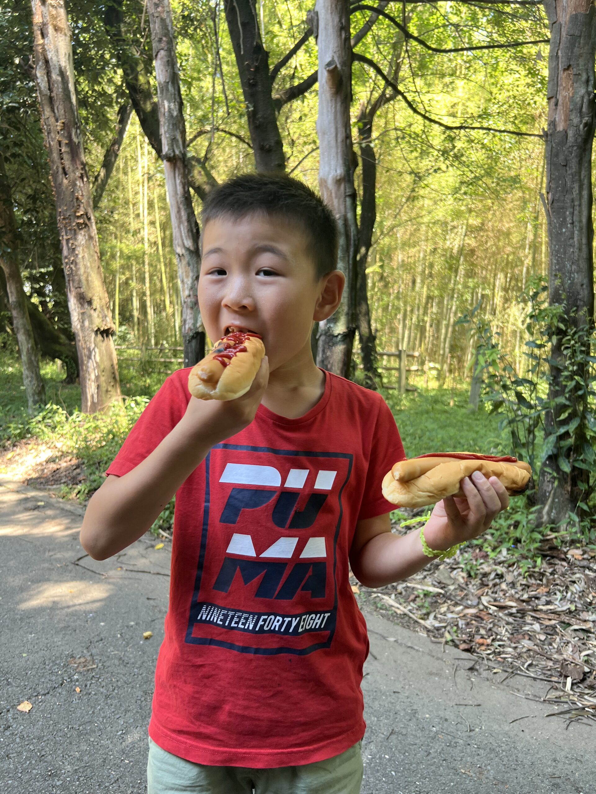 四日市で開催されたMiRAIサマスクで、男の子が自分の手で薪割りから火おこしをして作ったホットドッグに大きな口を開けてかぶりつく様子。夏休みならではの食育体験を全力で楽しんでいる瞬間。
