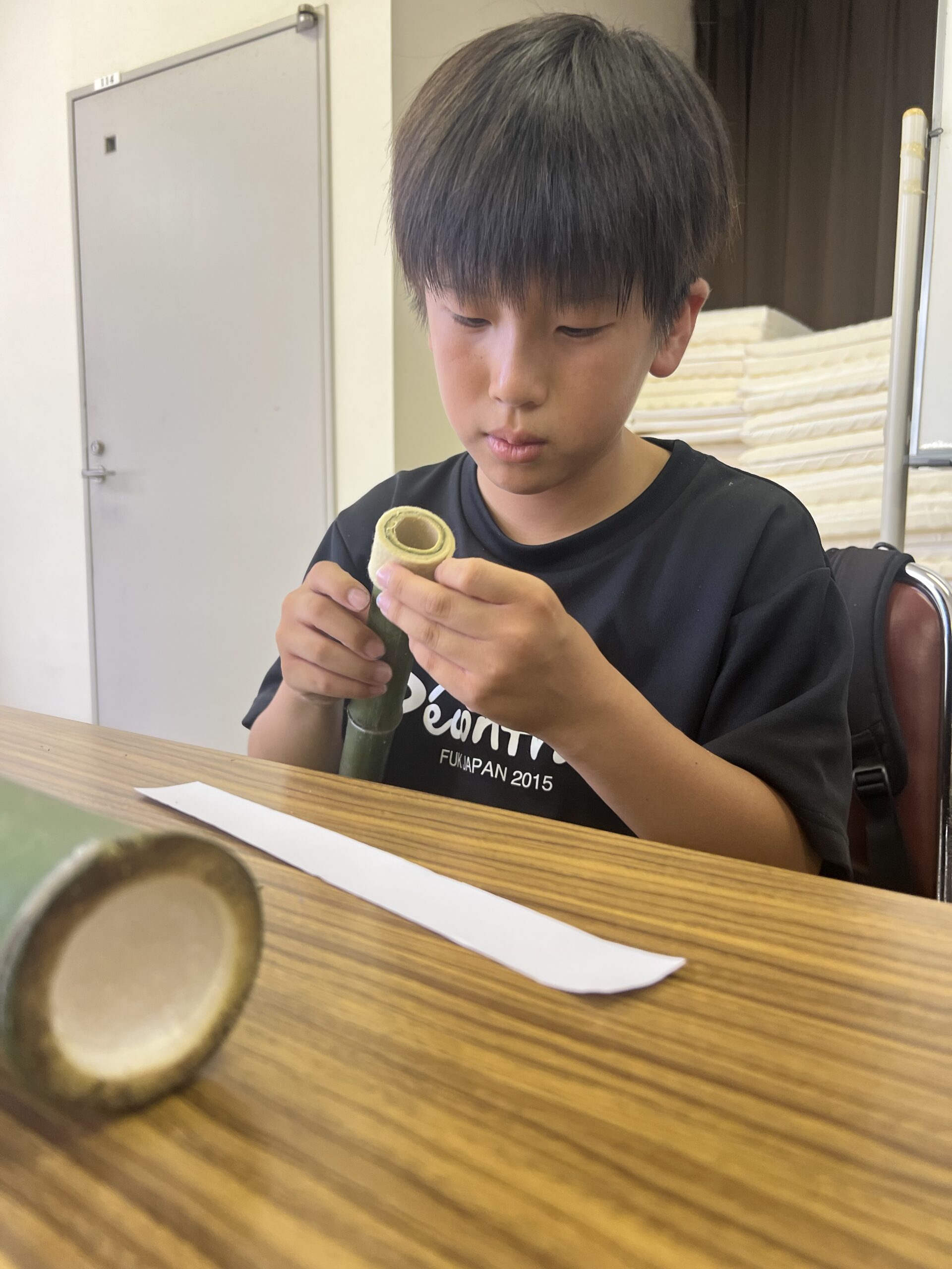 四日市で開催されたMiRAIサマスクに参加した男の子が、自分で切った竹を手に取り、ノコギリや工具を使って水鉄砲を作っている様子。夏休みの特別な創作体験で考える力と手先の器用さを育んでいる。