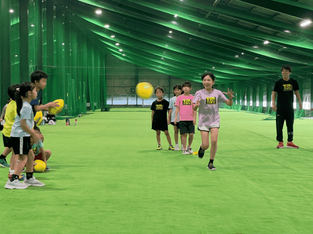 三重県四日市市総合スポーツスクールMiRAIで、子どもが笑顔で走りながらラグビーボールをキャッチする練習の様子