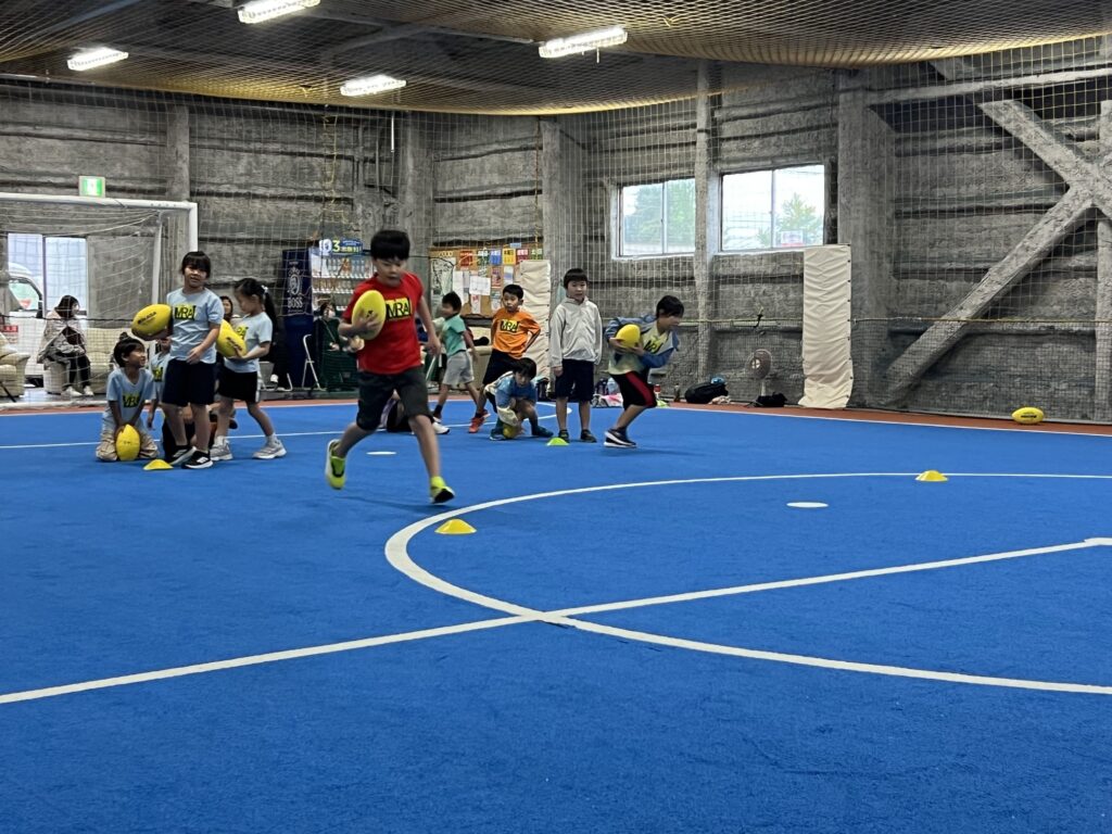 三重県菰野町総合スポーツスクールMiRAIで、小学生たちがゲーム形式のラグビーを楽しみながら学んでいる様子