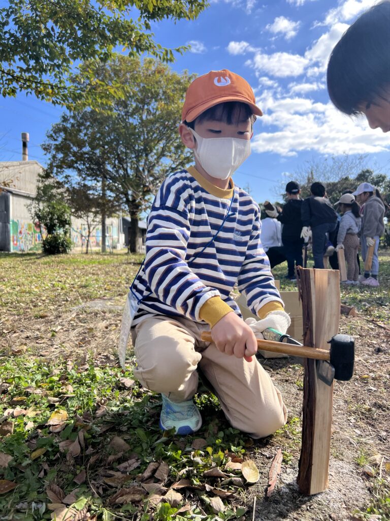 【年中〜小6対象】三重県北勢（四日市・菰野町）で人気の習い事。総合スポーツスクールMiRAIの野外体験で、子どもが集中力を発揮し薪割りに挑戦している様子。