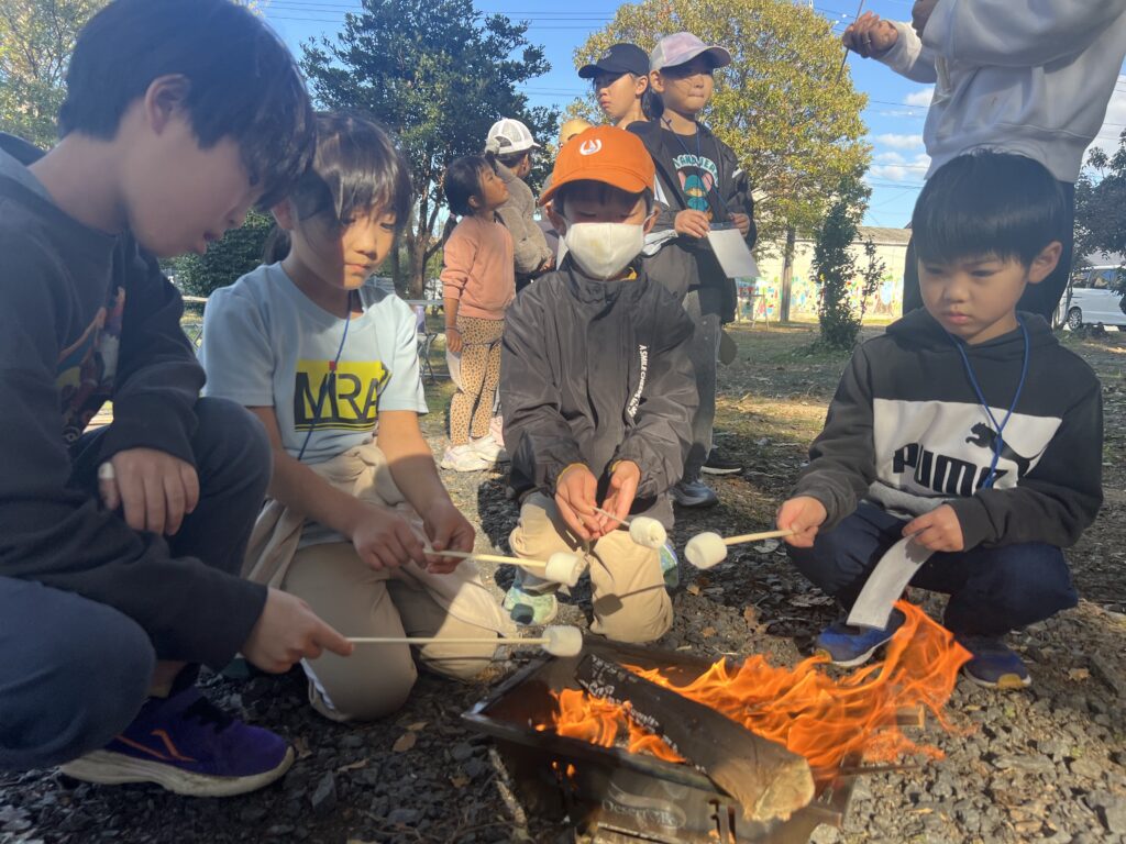 【年中〜小6対象】三重県北勢（四日市市・菰野町）の習い事。総合スポーツスクールMiRAIの野外体験で、子どもたちが焚き火を囲み焼きマシュマロを楽しんでいる様子。