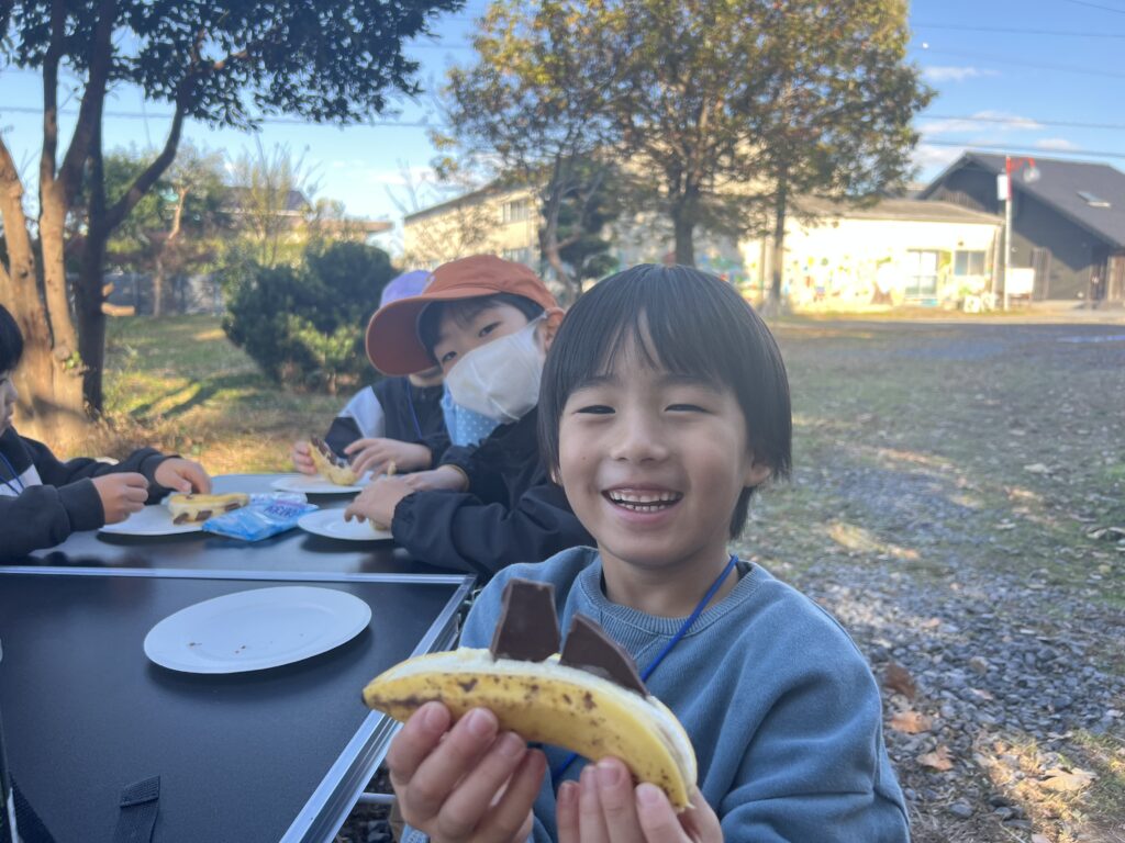 【年中〜小6対象】三重県北勢（四日市市・菰野町）の習い事。総合スポーツスクールMiRAIの野外体験で、自分で作ったバナナチョコを持ち、笑顔を浮かべる子ども。