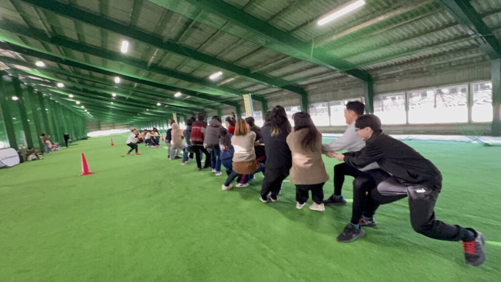 四日市・菰野町の総合スポーツスクールMiRAIの冬の運動会で、年中〜小学生の子どもたちと親御さんが一緒に綱引きを楽しんでいる様子