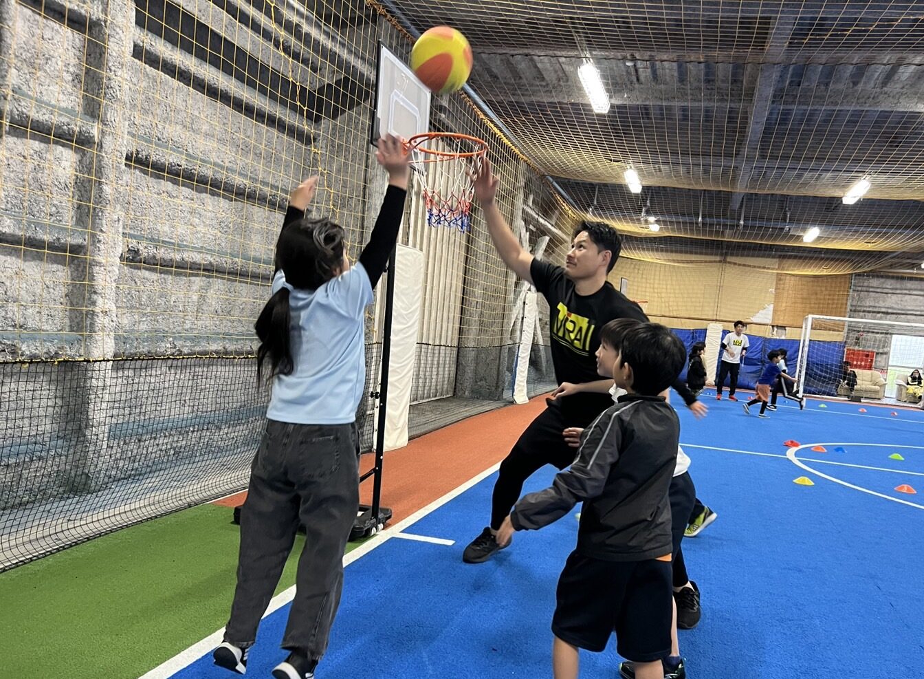 総合スポーツスクールMiRAIのバスケットボールで、先生と子どもたちが同じコートで一緒に体を動かしている様子