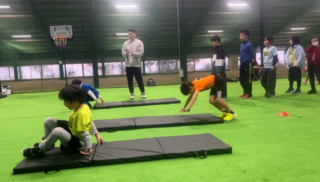 総合スポーツスクールMiRAIのバスケットボールクラスで、子どもたちが体の感覚を整えるためにマット運動を楽しんでいる様子