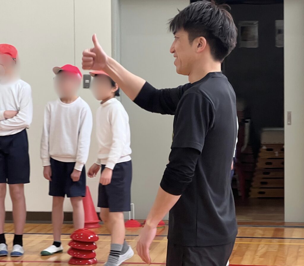四日市と菰野町で活動する子ども向けスポーツスクールの出前授業。小学生の動きを見て親指を立てる先生の様子