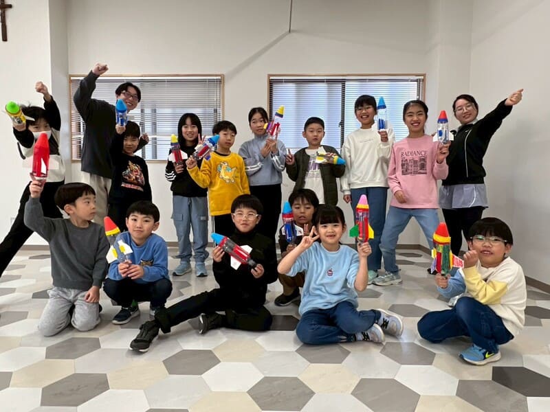 総合スポーツスクールMiRAIの科学教室に参加した子どもたちが、ペットボトルロケット体験を終えて笑顔で写る集合写真