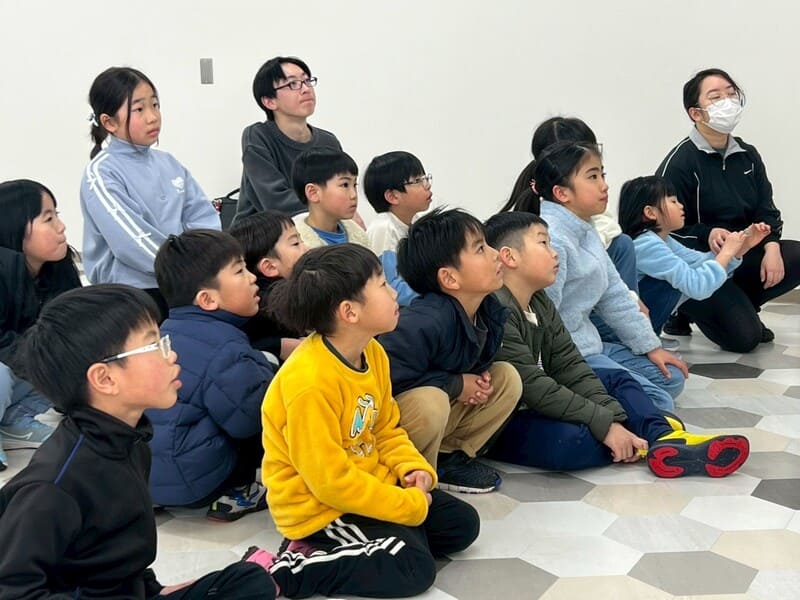 四日市メリノール学院で開催された総合スポーツスクールMiRAIの科学教室で、ペットボトルロケットづくりの説明を目を輝かせて聞く子どもたち